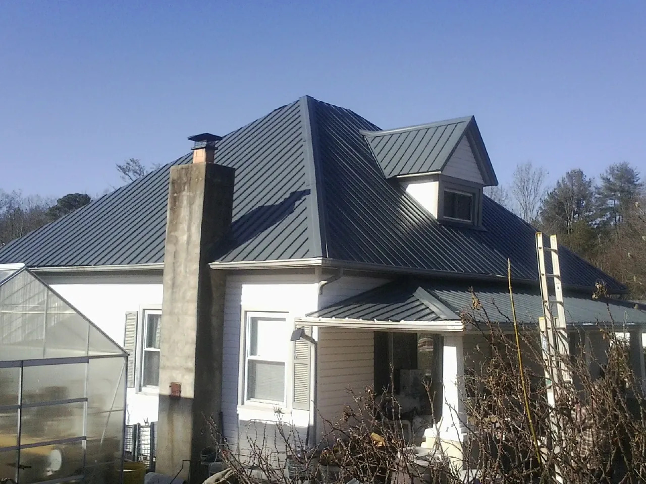 Dark blue standing seam metal roof on a white farmhouse with dormer — Slate & Tile Roof Repair by Roofing Brothers in Nashville